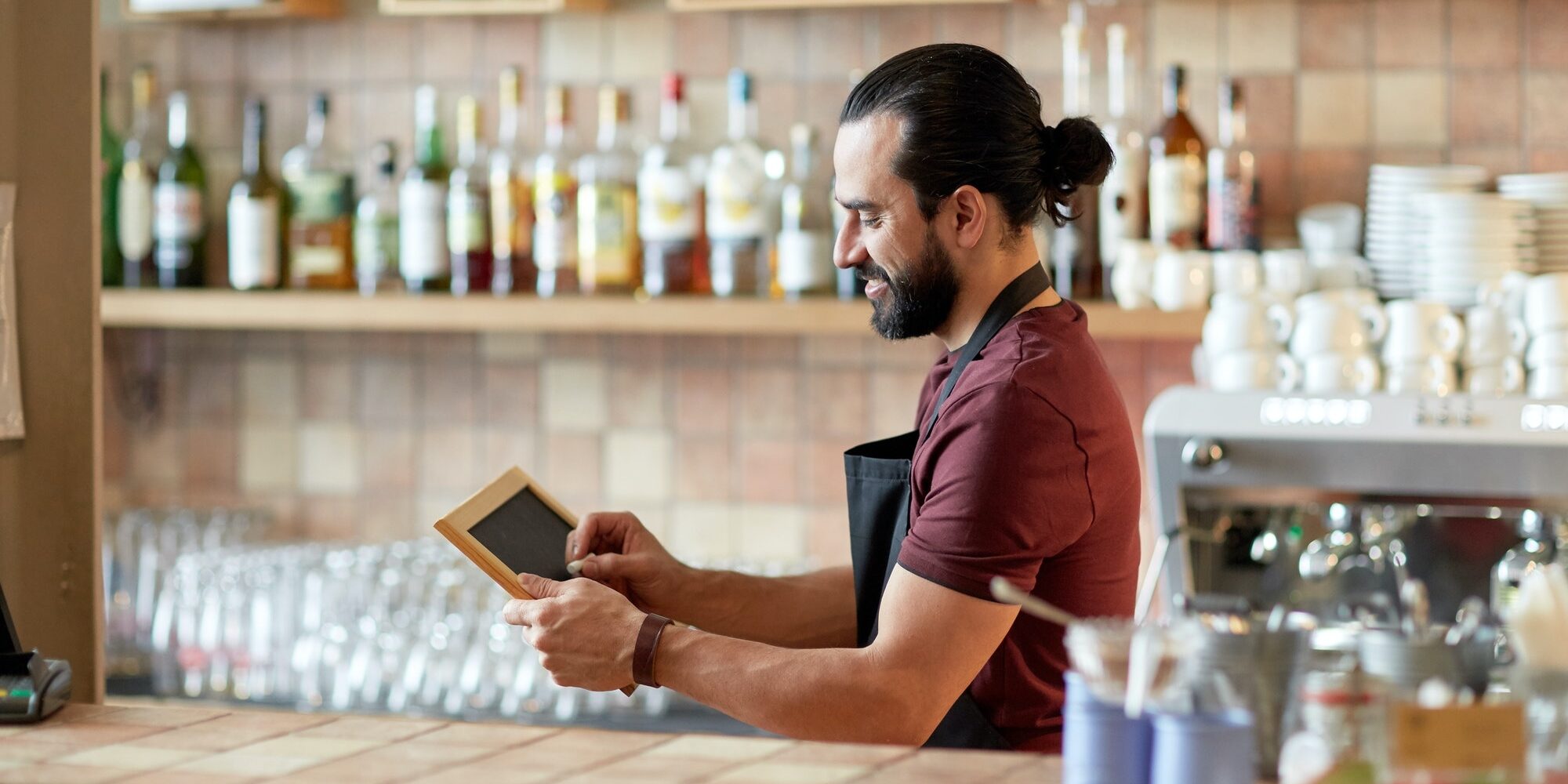 happy man or waiter with chalkboard banner at bar